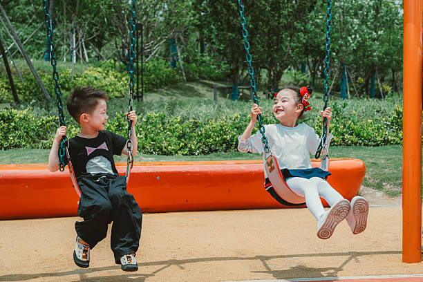 6-years-old Chinese children playing on a swing set in playground joyfully, The girl is wearing makeup of ancient China.