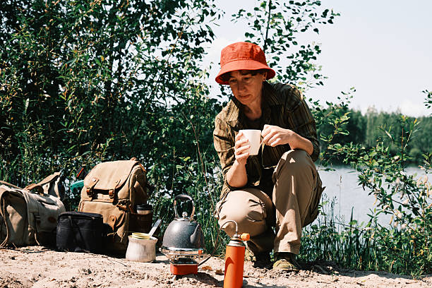 Single female hiker on sandy forest lake shore is drinking hot tea