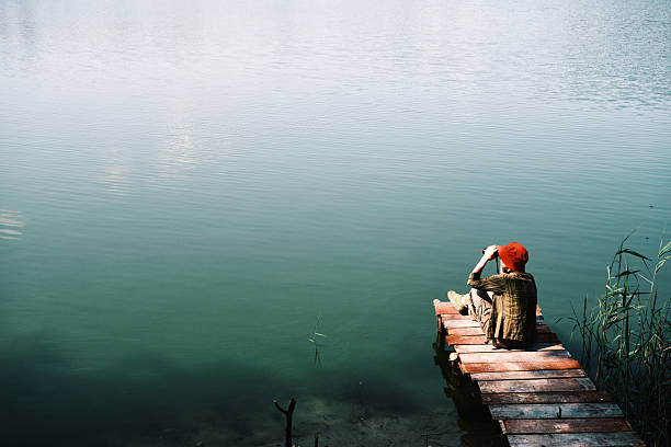 Single female birdwatcher is sitting above forest lake and watching through binoculars