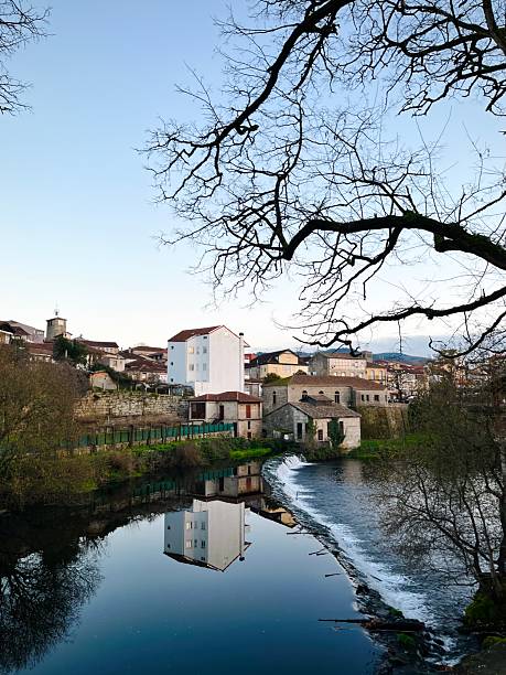 A tranquil riverside village scene showcasing calm waters reflecting buildings, lush greenery, and a serene environment. Ideal for portraying calmness, countryside living, or travel themes.