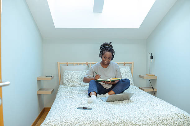 istock Woman wearing headphones writing notes while using a laptop on her bed 2219629223