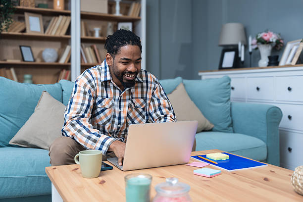 istock Young entrepreneur working from home, planning while reading suggestions on his laptop, enjoying a successful moment in a cozy living room, modern lifestyle and remote business concept. 2219629651