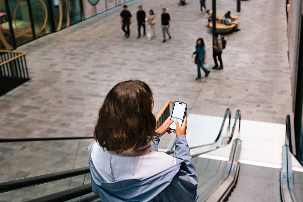 young woman use mobile app for investing checking stocks on escalator in the shopping mall berlin shopping centre stock pictures, royalty-free photos & images