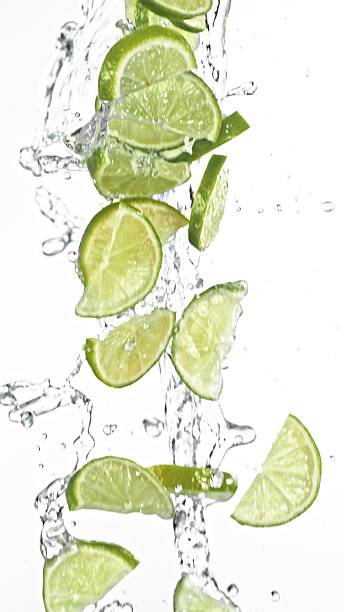 istock Fresh limes slices falling in water splashes, isolated on white background. 2219638029
