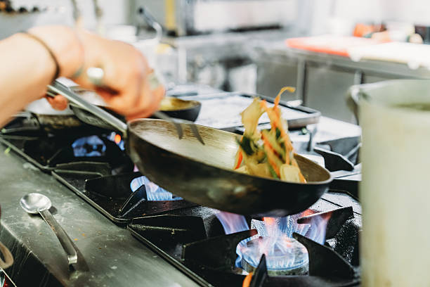 istock Chef tossing vegetables in a wok pan over a burning stove 2219640033