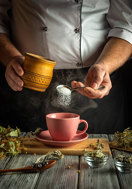 istock A chef skillfully pours sugar into a pink cup while surrounded by various dried herbs and natural ingredients on a wooden surface in a warm kitchen ambiance 2219640052