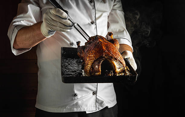 istock A chef in a white uniform and gloves holds a steaming roasted duck with a carving fork above a dark platter. The ambiance is cozy and inviting, emphasizing the culinary artistry 2219640178