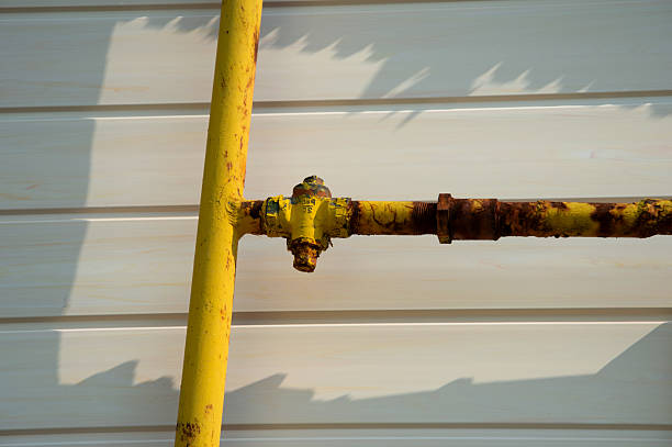 istock Old yellow pipe with rusty spots connected to a wall, highlighting aging infrastructure in an industrial environment during daylight hours 2219649382