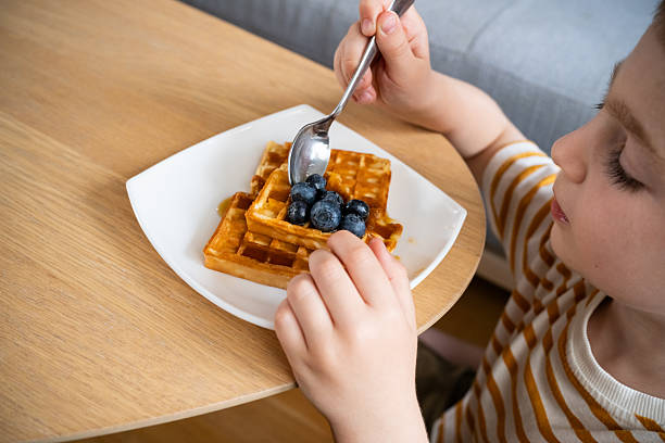 istock Child enjoying waffles with blueberries at a wooden table 2219649694