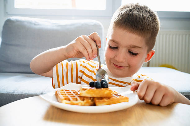 istock Boy enjoying waffles topped with fresh blueberries at the breakfast table 2219651096