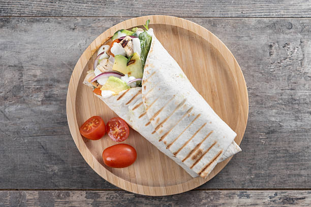 A delicious grilled chicken wrap with vegetables and avocado on wooden table