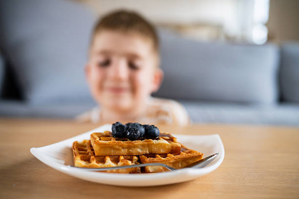 istock Boy smiling behind plate of blueberry topped waffles at a kitchen table 2219651635