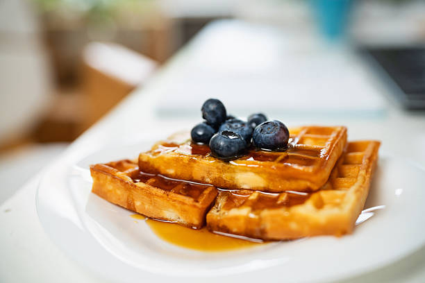 Delicious golden waffles topped with fresh blueberries and drizzled maple syrup for a delightful breakfast. The plate stands out on a bright and minimal dining table, capturing a cozy morning moment.