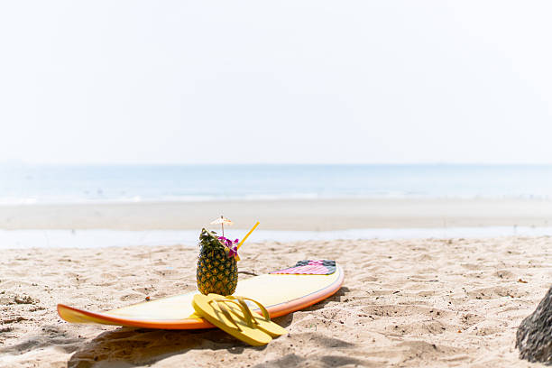 istock Beautiful decorated pineapple and flip-flops and surfboard left on the beach. Holidays, vacations, and summer vibes concept. 2219652348