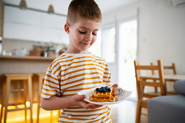 istock Smiling boy holding a plate with waffles topped with fresh blueberries in kitchen 2219652487