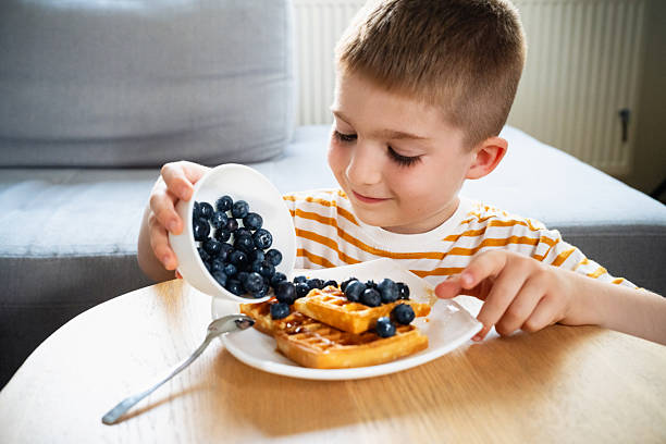 istock Young boy adding blueberries to waffles during breakfast at home 2219652571