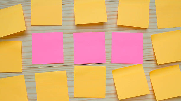 istock Pink sticky notes stand in the middle row surrounded by yellow notes, symbolizing individuality, uniqueness, leadership, or creative thinking on a wooden background. 2219652674