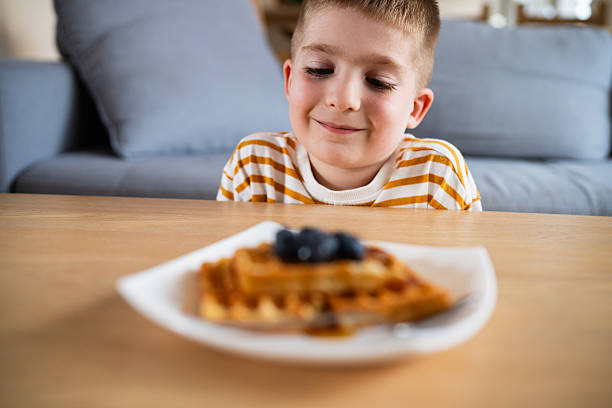 istock Young boy smiling at waffles topped with blueberries on a plate at a table 2219652741