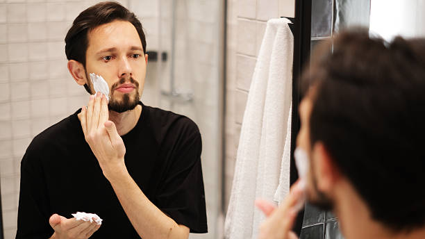 istock Young man applying shaving foam to cheeks while looking in mirror 2219654271