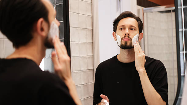 istock Young man applying shaving foam to cheeks while looking in mirror 2219654279
