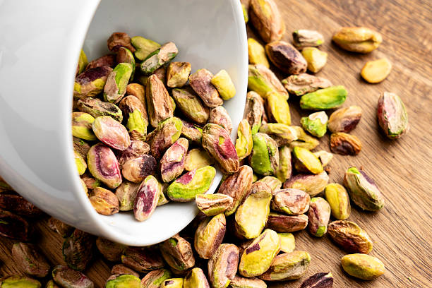 istock Shelled pistachio nuts spilled on wooden table from white cup 2219655860