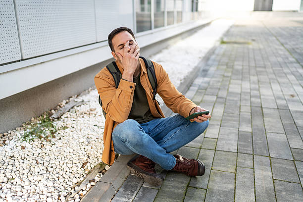 Tired tourist yawning while sitting and using his smartphone