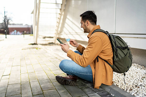 istock Young tourist paying online with credit card while sitting on sidewalk 2219658244
