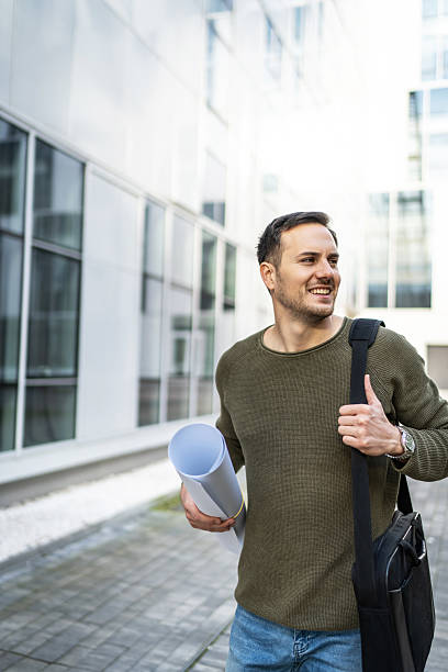 istock Smiling architect walking outside office holding blueprints 2219658297