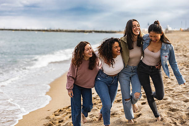 istock Four young women walking and laughing on the beach 2219660624
