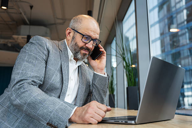 istock Mature Businessman Speaking on Smartphone While Working on Laptop in Co-working Area 2219664114