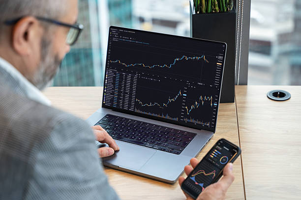 istock Man Analyzing Stock Market Data on Laptop and Smartphone in Modern Office 2219664228