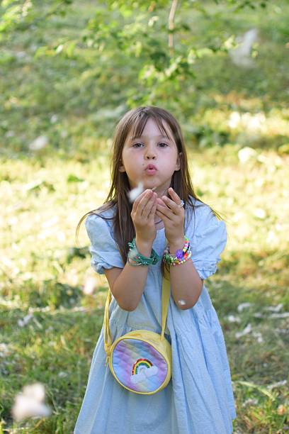 A serene close-up scene showing a hand holding a dandelion releasing seeds into the breeze, set against a natural green background, evoking feelings of serenity, connection with nature, and peaceful moments.