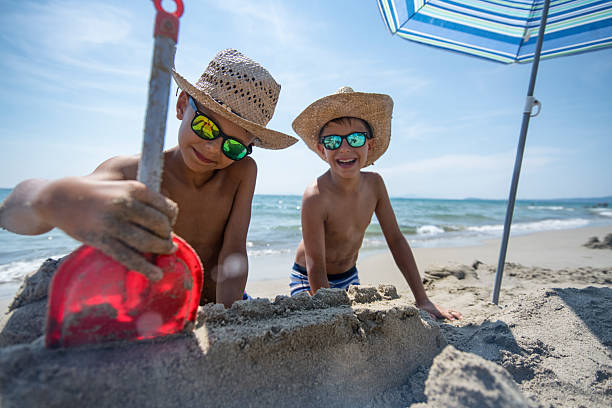 istock Two boys building sandcastles under a colorful beach umbrella on a sunny day 2219670126