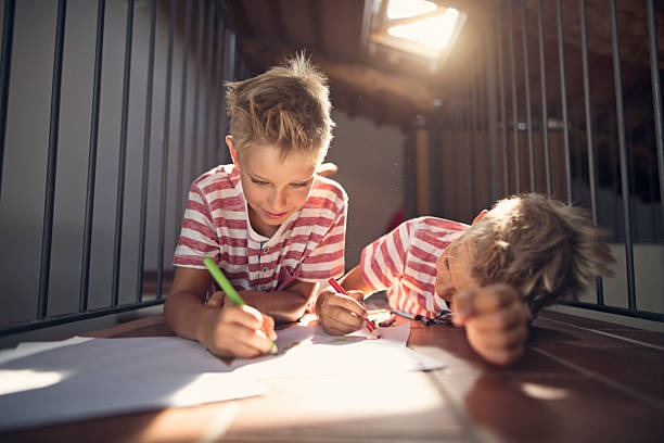 istock Two cute little boy twins drawing with crayons on attic near a skylight 2219670313