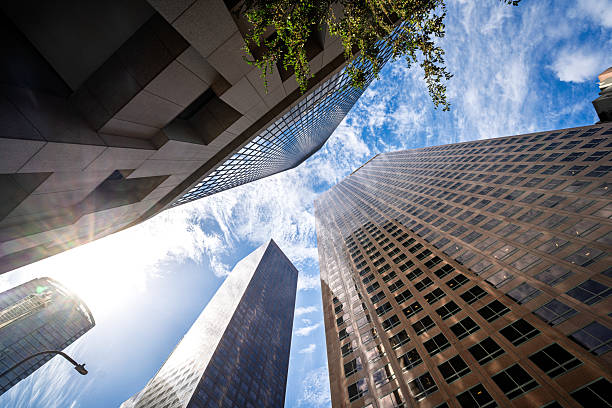 Modern glass skyscrapers in downtown Los Angeles rising into a vibrant blue sky with scattered clouds. Urban architecture and cityscape concept, captured from a low angle looking up.