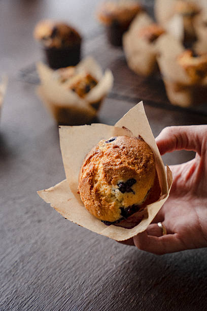 istock Hand Holding a Freshly Baked Blueberry Muffin on Rustic Background 2219674416