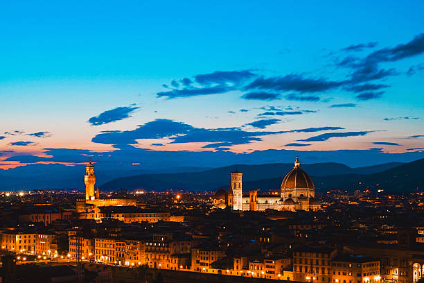 An early evening view of Florence from Piazzale Michelangelo, as city lights begin to glow beneath a fading blue sky. The iconic dome of Florence Cathedral rises gently above the rooftops, evoking the serene beauty of the Tuscan capital as day turns into night.