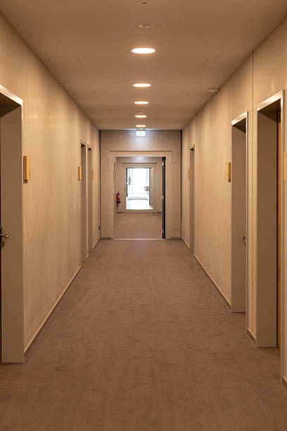 istock A long corridor features beige walls and carpeting, with doors on either side. Soft lights illuminate the path, leading to an open area at the end, creating a calm atmosphere 2219676406