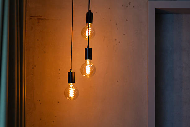 istock Three warm light bulbs hang from black cables, illuminating a textured wall in a contemporary room. The glow creates a cozy atmosphere, enhancing the space's design 2219676656