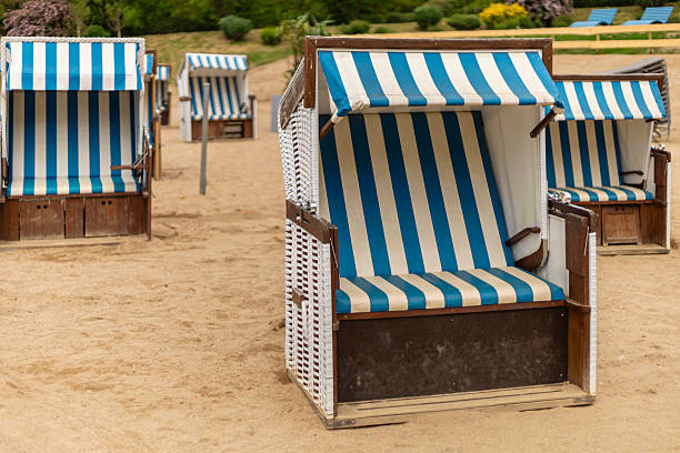 Blue and white striped beach chairs are arranged neatly on the sandy shore, creating a relaxing spot for visitors. The sun shines brightly, inviting leisure and enjoyment in this serene environment.