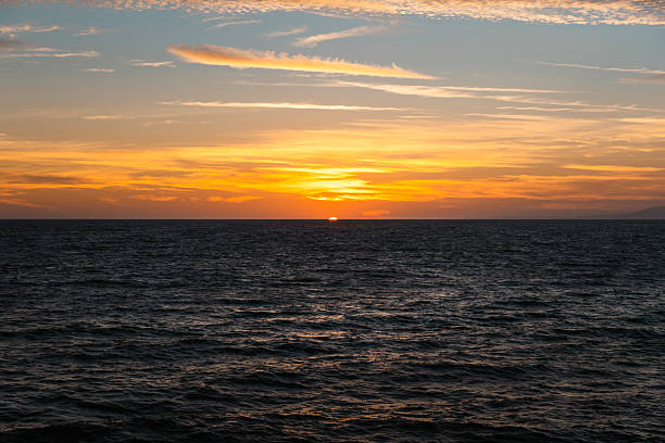 Stunning sunset view over the Pacific Ocean taken from the Venice Beach or Santa Monica coastline in Los Angeles, California. The image captures the last sliver of sun as it dips below the horizon, casting warm hues of orange, gold, and lavender across the sky. Gentle ocean waves fill the foreground, creating a serene and timeless composition ideal for themes of travel, nature, mindfulness, peace, and scenic beauty.