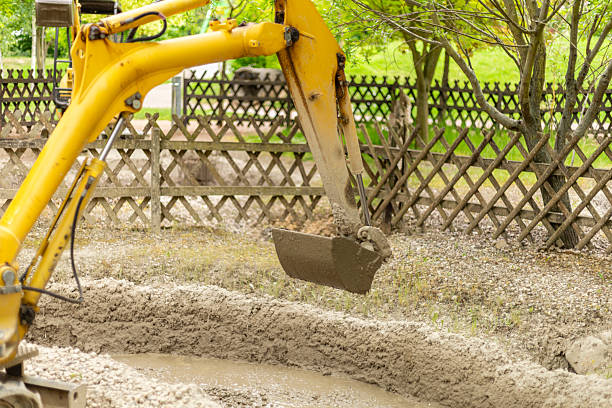 istock A yellow excavator performs earthmoving tasks in a construction zone surrounded by a wooden fence. The machinery lifts a bucket filled with soil under clear skies 2219677418