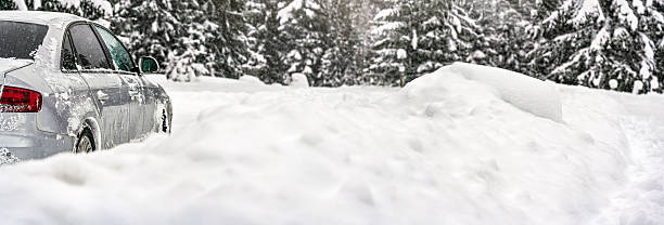istock Silver car covered with ice parked on deep snow covered road, detail view from behind, blurred trees background empty space for text right side 2219678356