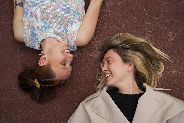 Two young women lying on the ground, gazing at each other with smiles, sharing joyful moments together and embracing the warmth of their friendship and connection