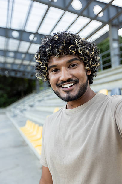istock A young man smiles into the camera while video calling at the stadium, in a casual setting with seats visible in the background. 2219691395