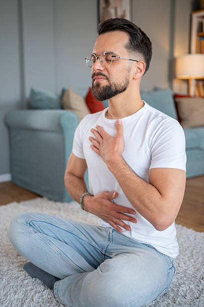 istock Young adult man practicing deep breathing exercise at home 2219695646