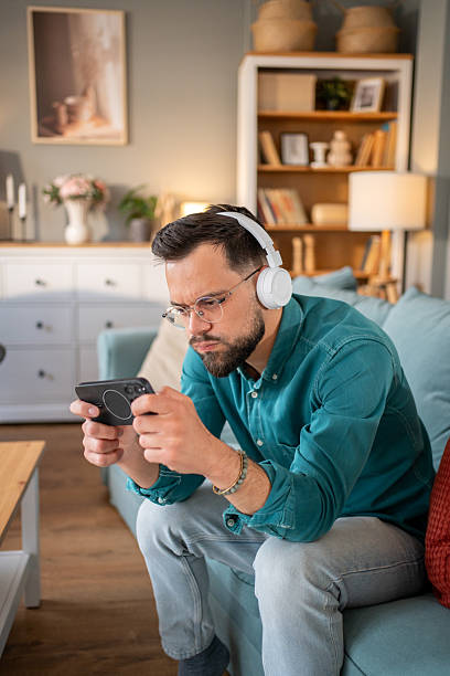 istock Young man playing videogames on mobile phone while wearing headphones at home 2219696069