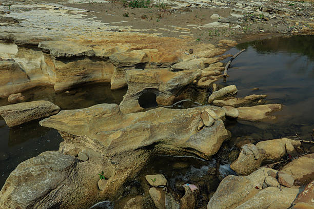 A naturally formed rock arch in a shallow riverbed with water gently flowing through it. Captured in Indonesia, this geological formation is shaped by erosion and time, highlighting the power of nature and the beauty of natural structures.