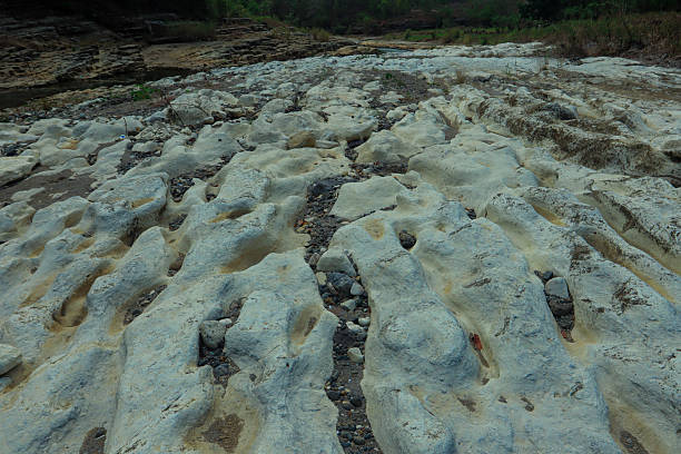 A dried-out riverbed showing natural erosion patterns in the rocky terrain, with scattered pebbles and exposed geological formations. Captured in Indonesia, this landscape highlights environmental changes, seasonal drought, and the impact of nature over time.