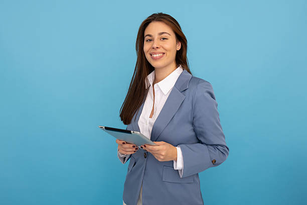 istock Professional businesswoman smiling, holding tablet against blue workspace backdrop 2219703783